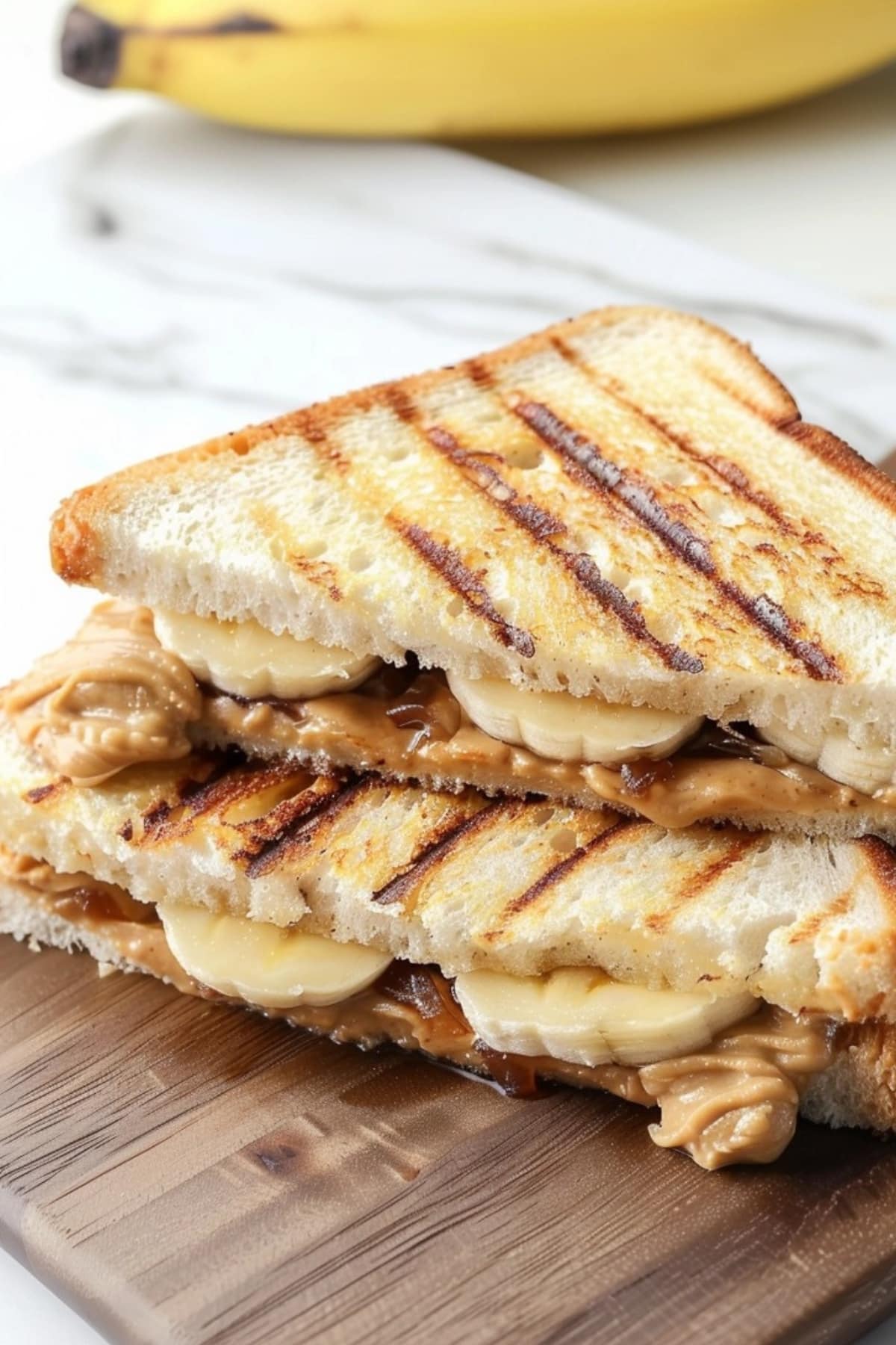Grilled peanut butter and banana sandwich stack on a wooden board.